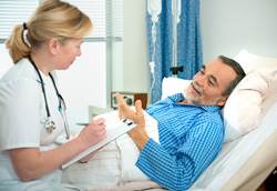 A nurse listens to a male patient lying in a hospital bed.